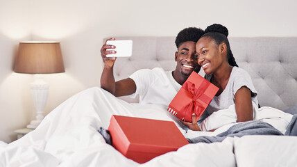 Selfie, happy and black couple in home with gift, smile or celebration of relationship on Valentines day. People, love or social media picture in bed with present for anniversary, romance or surprise
