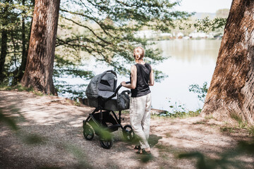 Rear view of casually dressed mother walking with baby stroller in Koseski bajer city park in...