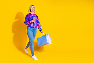 Full size photo of pretty young girl walk hold device shopper wear trendy colorful blue outfit isolated on yellow color background