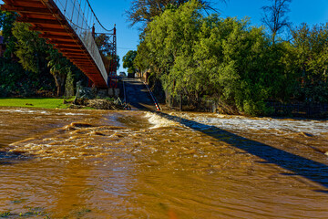 Flooded river crossing adjacent to pedestrian suspension in residential area Oudtshoorn, Western...