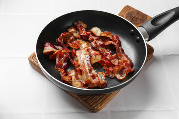 Delicious bacon slices in frying pan on white tiled table