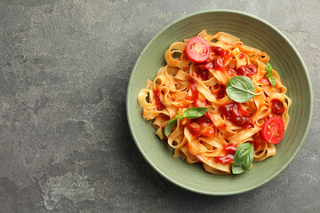 Delicious pasta with tomato sauce and basil in bowl on grey textured table, top view. Space for text