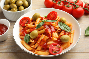 Delicious pasta with tomato sauce, basil and olives in bowl on wooden table, closeup