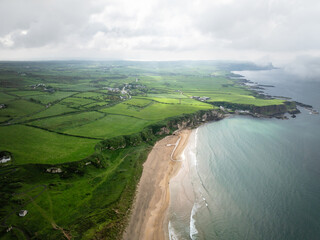 Küste mit Klippen und Felsen und Stränden und Licht und grünen Wiesen von Nordirland von oben 
