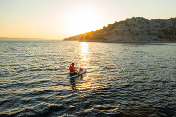 Man in orange vest navigating on the paddleboard in the sea at sunset.