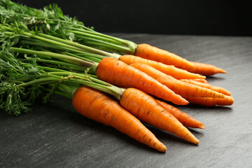 Tasty ripe juicy carrots on dark gray textured table, closeup