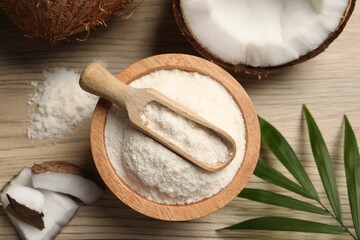 Fresh coconut flour in bowl, scoop, nut and palm leaf on wooden table, flat lay