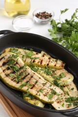 Tasty grilled zucchini slices in dish on white table
