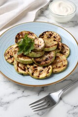Tasty grilled zucchini slices with parsley served on white marble table