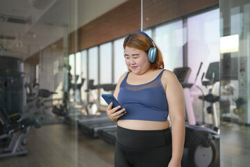 Fototapeta premium Female with smart phone&nbsp;after workout at Gym. Obese asian woman watching online workout training class.