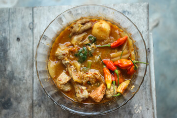 Seblak is a typical Indonesian dish with a savory and spicy taste. Made from wet crackers cooked with vegetables, sausage, eggs. a bowl of seblak on a wooden table.