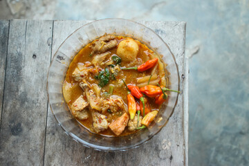 Seblak is a typical Indonesian dish with a savory and spicy taste. Made from wet crackers cooked with vegetables, sausage, eggs. a bowl of seblak on a wooden table.