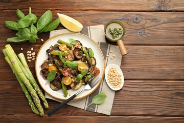 Delicious salad with grilled vegetables, basil, pesto sauce, pine nuts and fork on wooden table,...