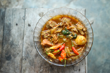 Seblak is a typical Indonesian dish with a savory and spicy taste. Made from wet crackers cooked with vegetables, sausage, eggs. a bowl of seblak on a wooden table.