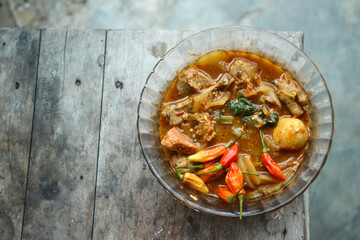 Seblak is a typical Indonesian dish with a savory and spicy taste. Made from wet crackers cooked with vegetables, sausage, eggs. a bowl of seblak on a wooden table.