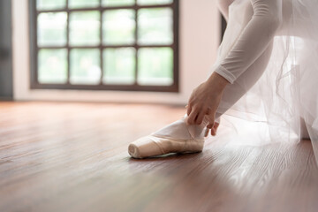 Ballerina in ballet shoes. Asian girl tying ribbons of toe shoes. ballet dancer preparing and wearing ballet shoes in dance studio prepares for a rehearsal.