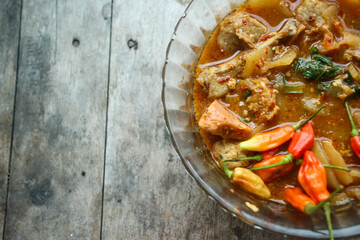 Seblak is a typical Indonesian dish with a savory and spicy taste. Made from wet crackers cooked with vegetables, sausage, eggs. a bowl of seblak on a wooden table.