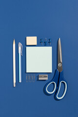 Empty blue paper sheet with pen, pencil, pins, scissors and clips on a blue background. Office and...