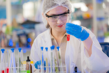 female scientist Experimenting through tubes of chemical liquids and plant samples. In a laboratory with test samples in the background in a modern laboratory By testing safely and cleanly.