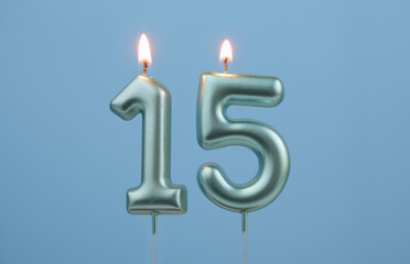 Burning blue birthday candles on blue background, number 15