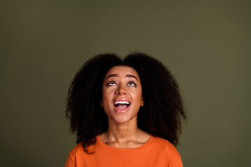 Photo of impressed nice woman with perming coiffure dressed orange shirt look up at logo empty space isolated on dark khaki background