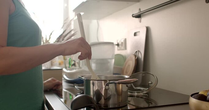 A person skillfully stirs pot in modern kitchen, showcasing the art home cooking and culinary talent She uses a spoon to stir the food in the pan.