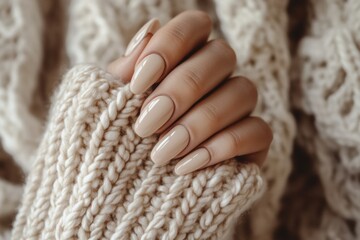 Close up of a woman's elegant, nude manicured nails holding a cozy beige knitted sweater. Generated AI