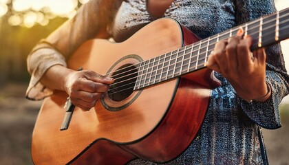 Fototapeta premium Closeup of guitarist hand playing guitar. Musical instrument concept. Outdoors and Leisure theme. Selective focus on left hand. Vintage country folk guitar with music singer. Close up entertainer hand