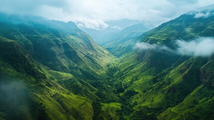 Fototapeta premium Overhead shot of a lush green valley nestled between mountain ridges with plenty of copy space in the sky