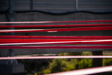 A detailed close-up of tensioned red straps securely fastened with a metal hook on a gravel surface, demonstrating precision and strength in securing elements.