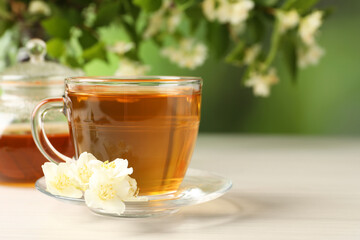 Hot jasmine tea in cup and flowers on white wooden table, space for text