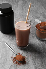Delicious protein shake in glass, powder, spoon and plastic bottle on grey table