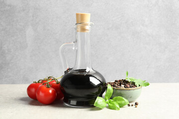 Balsamic vinegar in glass jug, tomatoes, herbs and spices on gray textured table