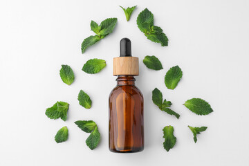 Bottle of essential oil and mint isolated on white, top view