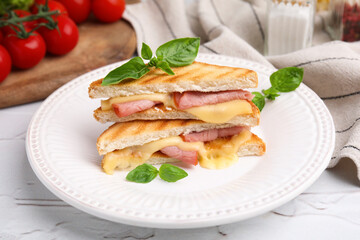 Pieces of toasted bread with melted cheese, ham and basil on white table