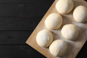 Raw dough balls on black wooden table, top view. Space for text