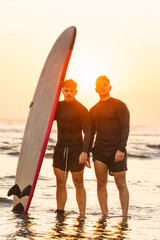 Two male surfers on the shore of the beach at sunset