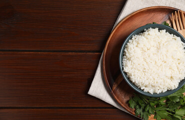 Delicious boiled rice served with parsley on wooden table, top view. Space for text