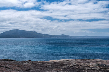 Two Peoples Bay in Australia features a tranquil wooden walkway through coastal vegetation and pristine waters under a bright, partly cloudy sky. Perfect for travel and nature photography enthusiasts.
