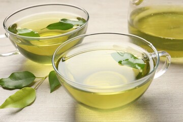 Refreshing green tea in cups and leaves on wooden table, closeup