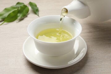 Pouring refreshing green tea into cup at wooden table, closeup