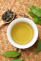 Refreshing green tea in cup, spoon and leaves on table, flat lay