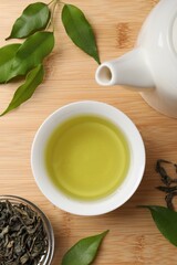 Refreshing green tea in cup, teapot and leaves on wooden table, flat lay
