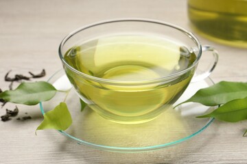 Refreshing green tea in cup and leaves on wooden table, closeup