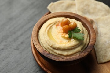 Delicious hummus with olive oil, chickpeas in bowl and pita on grey table, closeup