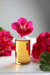 Bottle of geranium essential oil and beautiful flowers on white wooden table