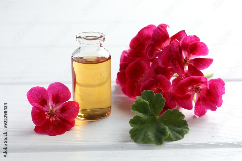 Wall mural bottle of geranium essential oil and beautiful flowers on white wooden table, closeup