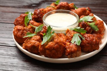 Baked cauliflower buffalo wings with parsley and sauce on wooden table, closeup