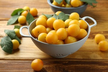 Tasty ripe plums and leaves in colander on wooden table, closeup