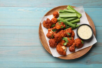 Baked cauliflower buffalo wings with celery and sauce on light blue wooden table, top view. Space for text